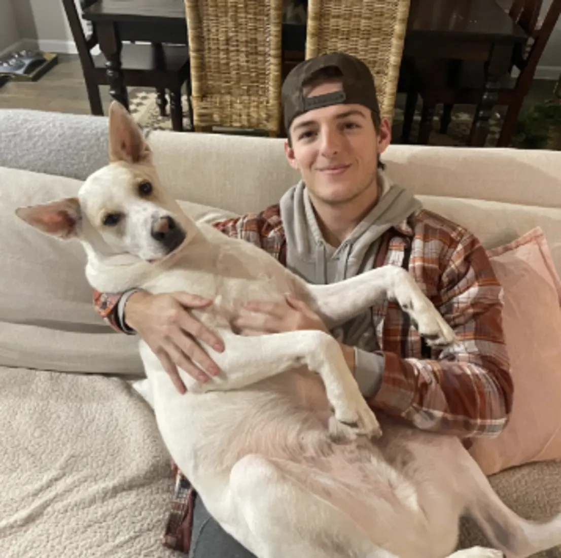 Man in cap holding small dog close to his face